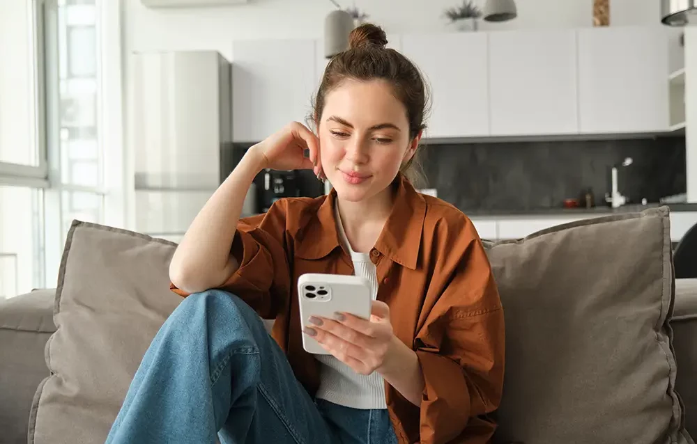 portrait-happy-young-brunette-woman-sitting-sofa-with-smartphone-reading-notification